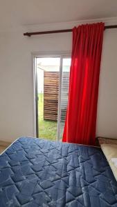 1 dormitorio con 1 cama con cortina roja y ventana en Contenedor a metros del mar en Quequén