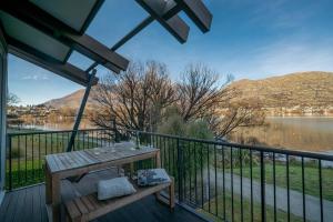 a wooden bench on a deck with a view of a lake at Marina Gem - Lakefront 3 Bedroom Apartment in Queenstown