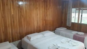 Duas camas num quarto com paredes de madeira e uma janela em Chalé Estância da Mata Nobres MT em Nobres
