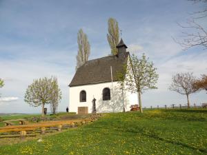 een kleine witte kerk op een heuvel met een bankje bij Ferienwohnung Vogt in Mertloch