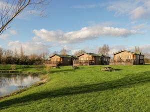 eine Gruppe von Häusern auf einem Feld mit einem Teich in der Unterkunft Harvester Lodge in Puxton