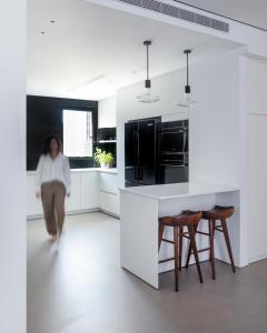 a woman walking through a kitchen with white cabinets at 12 Shimon HaTzadik - By Beach Apartments TLV in Tel Aviv