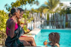 Pili Pili Uhuru Beach Hotel في جامبياني: وجود سيدتان جالستان بجانب حمام السباحة تاكلان الطعام