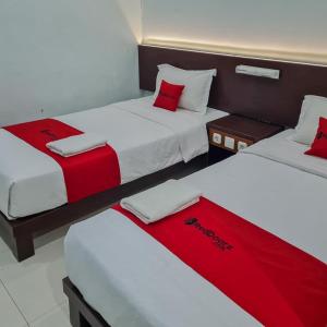 drie bedden in een kamer met rode en witte lakens bij RedDoorz Plus at Hotel Royal Palangka Raya in Palangkaraya