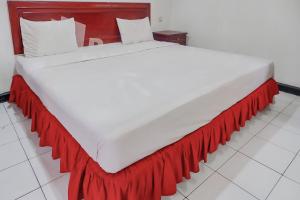 a large white bed with a red skirt on it at Graha Sartika Hotel RedPartner in Bandung