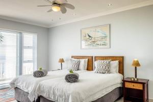 two beds in a white bedroom with a ceiling fan at Driftwood Beachfront Manor - Shelley Point in St Helena Bay