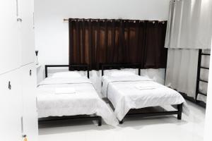 two beds in a room with white walls and curtains at Munruk Hostel in Prachuap Khiri Khan