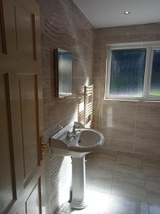 La salle de bains est pourvue d'un lavabo blanc et d'une fenêtre. dans l'établissement Impeccable 5-Bed Cottage in fahan buncrana, à Buncrana