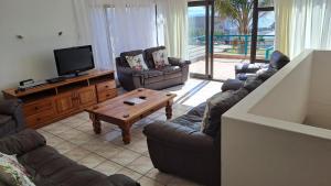 a living room with couches and a flat screen tv at Villa @ 19 Palm with spectacular sea views in Jeffreys Bay