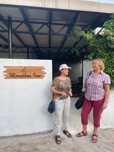 dos mujeres de pie junto a una pared con una señal en Mandhoo Inn en Mandhoo