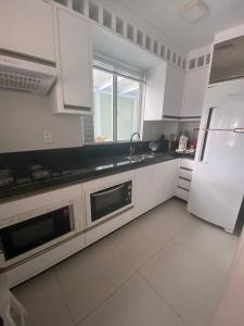 Una cocina con gabinetes blancos y un refrigerador blanco. en Apto Almeida e Moraes 2 Quartos e Churrasqueira Perto do Mar, en Balneário Camboriú