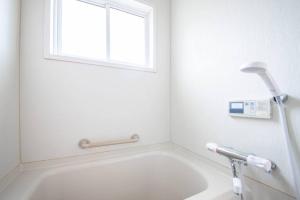 een witte badkamer met een bad en een raam bij Otaru Shikkui Cottage in Kita-hamachō