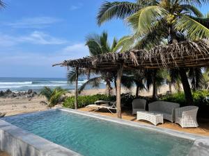 a swimming pool with a straw umbrella and a beach at Quinta Feliz Troncones in Troncones