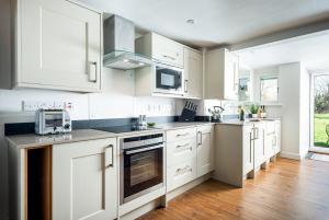 a white kitchen with white cabinets and a microwave at Lakeside property with spa access on a nature reserve Ruby Cottage MV04 in Somerford Keynes