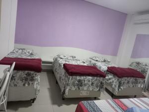 three beds in a room with purple walls at Hotel Farrapos in Porto Alegre