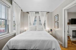 a white bedroom with a large white bed with windows at Elegant and Historic Getaway Close to Everything in Oklahoma City