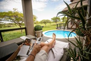 un hombre tirado en un porche leyendo un libro al lado de una piscina en Jamala Madikwe, en Reserva de Madikwe