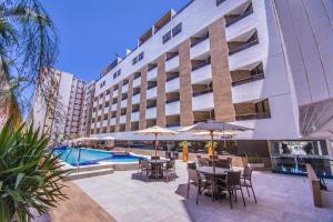 un patio del hotel con mesas y sombrillas y una piscina en Gold Flat Cabo Branco, en João Pessoa