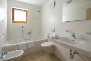 La salle de bains blanche est pourvue d'une baignoire, de toilettes et d'un lavabo. dans l'établissement Ciasa Vilin, à Corvara in Badia
