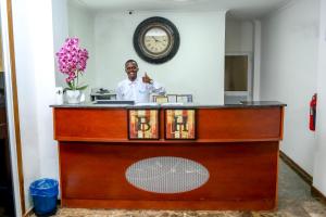 a man standing behind a counter with a clock on the wall at Brisotel - Beira Mar in Luanda