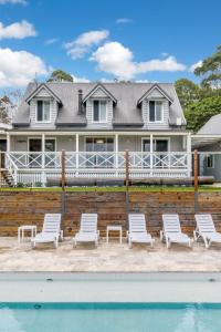una casa con sillas blancas y piscina en The Estate Byron Bay, en Bangalow