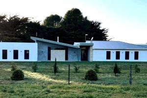 东南金斯顿White Hut on Golflinks的一片田野上的白色建筑,前面有灌木丛