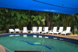 a swimming pool with white chairs and a blue roof at Hidden Valley Holiday Park Darwin in Darwin