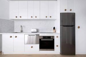 una cucina con armadietti bianchi e frigorifero nero di Studio Bondi Beach a Sydney