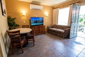 Albury Georgian Motel & Suites في البوري: غرفة معيشة مع طاولة وأريكة وتلفزيون