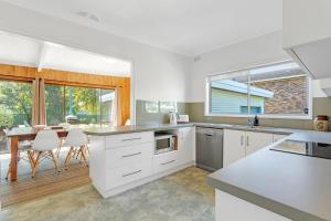 a kitchen with white cabinets and a dining room with a table at Berry by The Bay in Vincentia +5 photos