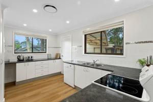 ビンセンチアにあるFamily Tides Beach Escapeの白いキャビネットとシンク付きのキッチン、窓2つが備わります。