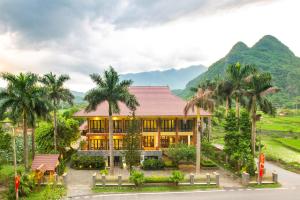 a house with palm trees and a mountain in the background at Mai Chau Lodge in Mai Châu