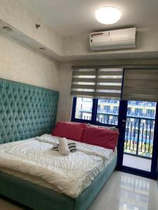 Schlafzimmer mit einem Bett mit einem blauen getufteten Kopfteil und Fenstern in der Unterkunft Sea Residences JO Alano's Place in Manila