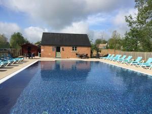 a swimming pool with blue chairs and a house at The Stables, Lower Mill Estate in Somerford Keynes