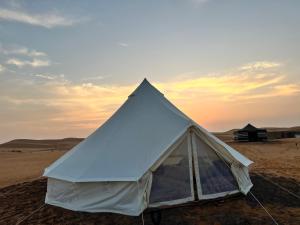 una tienda en el desierto con una puesta de sol en el fondo en Desert Private Camps -ShootingStar Camp, en Shāhiq
