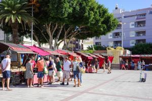 a group of people standing around a market with red umbrellas at Medano Nest Hostel in El Médano