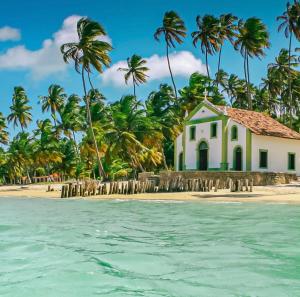 a church on a beach with palm trees at Tamandaré Praia Hotel in Tamandaré