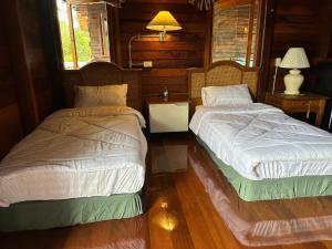 two beds in a room with wood floors and windows at พิมพ์วนา เขาใหญ่ in Nakhon Ratchasima