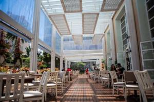 un restaurant avec des tables et des chaises blanches et des personnes se promenant dans les environs dans l'établissement IL Campanario - Suíte, à Florianópolis