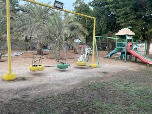 un parque infantil con columpios y un tobogán en Big Guest House - استراحة كبيرة en Al Ḩamīdīyah