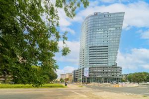 wysoki szklany budynek z parkingiem przed nim w obiekcie Apartament Tokyo HANZA POOL w Szczecinie