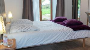 uma cama branca com almofadas roxas e uma janela em Domaine de la Basse Orme em Les Iffs