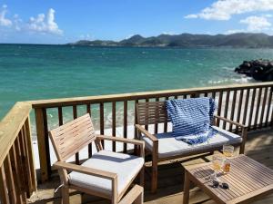 2 Stühle und ein Tisch auf einem Balkon mit Meerblick in der Unterkunft La Plage Bleue feet in the water with swimming pool in Baie Nettle