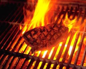 a steak is cooking on a grill with flames at Hotel Deutsches Haus und Restaurant Olympia in Magdeburg