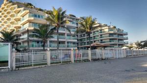 une clôture blanche devant un bâtiment planté de palmiers dans l'établissement Meu Resort no Recreio - RJ, à Rio de Janeiro