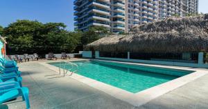 Hotel Los Veleros Santa Marta في سانتا مارتا: مسبح وكراسي وسقف من القش