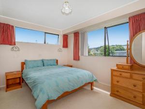 a bedroom with a bed and a mirror and windows at Treasure on Chestnut - Tairua Holiday Home in Tairua