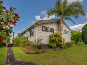 a white house with a palm tree in the yard at Treasure on Chestnut - Tairua Holiday Home in Tairua