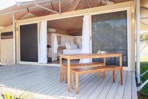 a wooden deck with a table and a bed at Crowdy Bay Eco Resort in Harrington