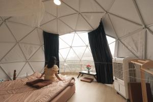 eine Frau auf einem Bett in einem Zimmer mit einem großen Fenster in der Unterkunft Dome บ้านสกายพฤกษ์ in Mon Jam